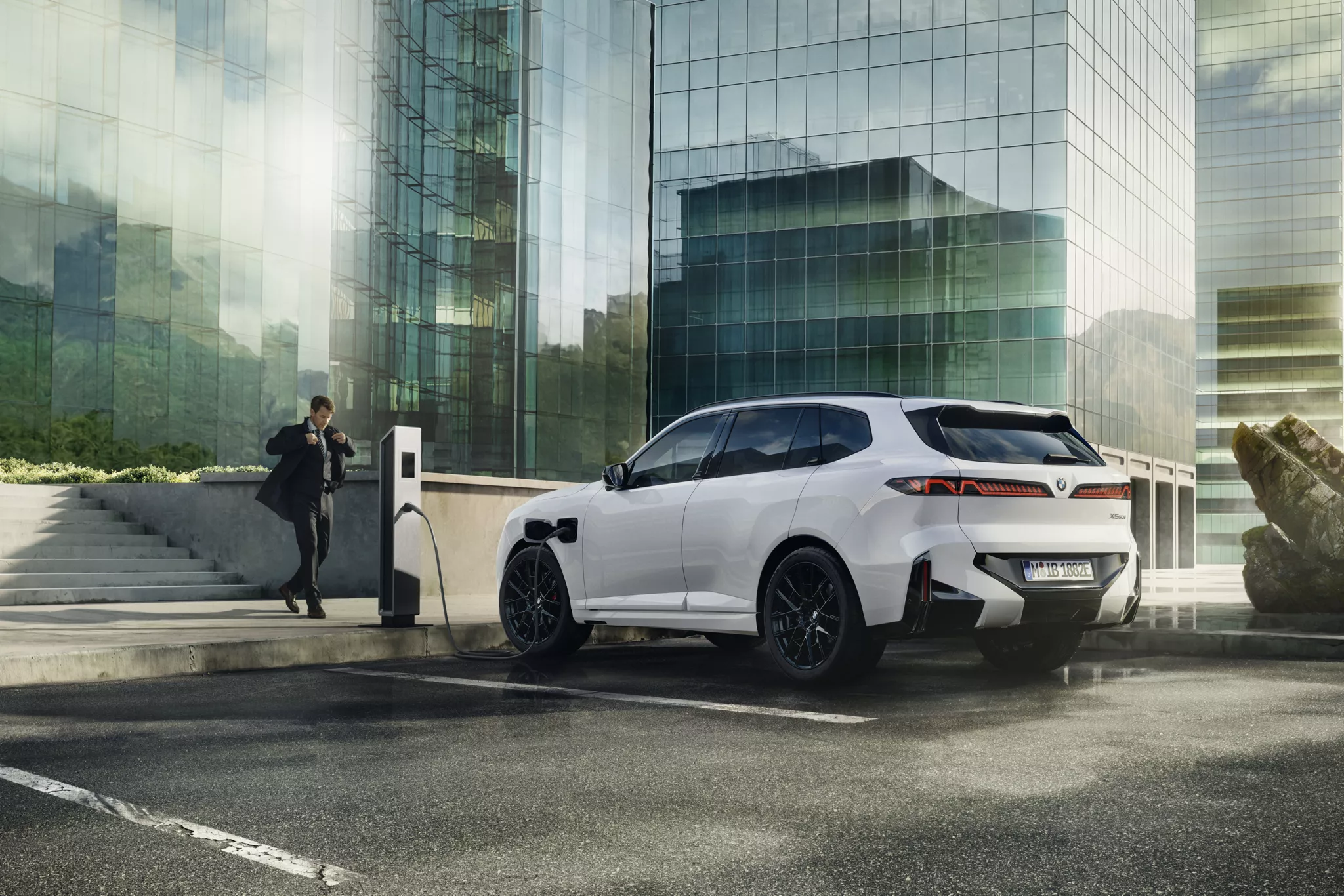 Egy BMW modern, az óceánra néző teraszon töltődik, egy sziklaalakzat mellett.